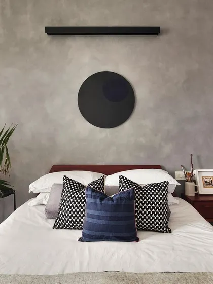 A close-up of the minimalist bedroom styling in the 'Rustic Minimal' project. The circular artwork and linear light fixture complement the cement-textured wall, creating a balanced and artistic composition.