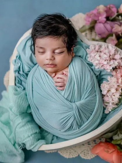 A little blossom in blue. The combination of the soft swaddle and the delicate flowers creates a serene and artistic portrait.