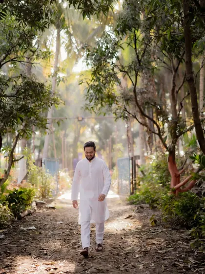 A candid shot of the groom walking through a grove of trees, a quiet moment before the Haldi festivities.