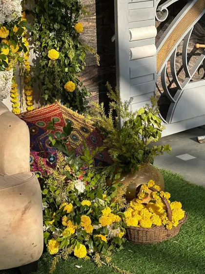 A detailed shot of the side of the Haldi stage, showing the combination of marigold baskets, greenery, and a decorative umbrella against the brick wall.