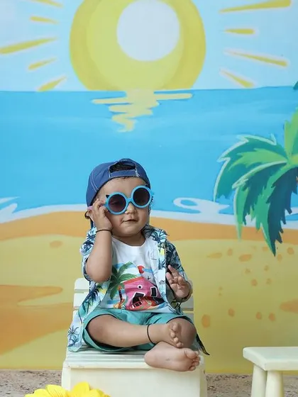 The toddler looks stylish with his blue sunglasses, adding a pop of color to the beach scene.