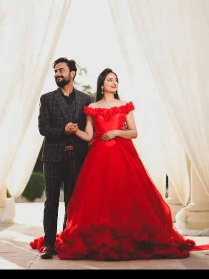 A full length view of our off shoulder red ball gown, paired with a stylish checkered suit for the groom to be.