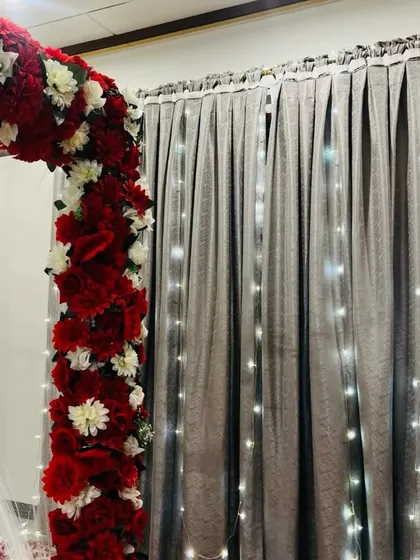 A close-up of the floral arrangement on the bed's four-poster frame. The dense red and white flowers are beautifully complemented by the warm glow of fairy lights.