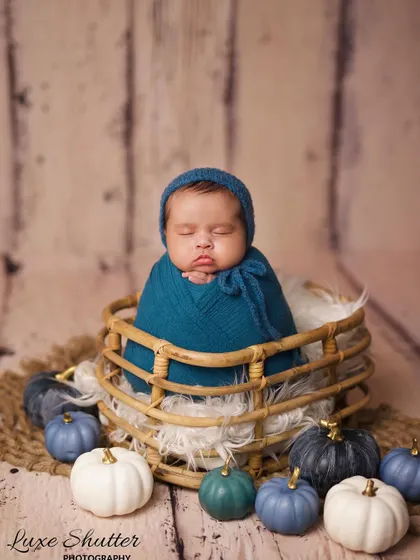 A close-up of the autumn pumpkin theme, showing the baby's sweet expression while sleeping. The textures of the wrap and basket add depth to the photo.