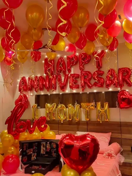 A one-month anniversary celebration. This romantic room setup features red and gold balloons, 'Happy Anniversary' and '1 Month' foil letters, and a special photo explosion box.