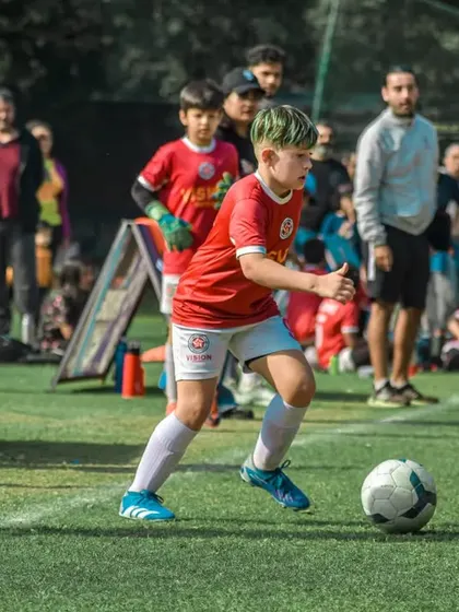 A young player with dyed green hair dribbles the ball with intense focus.