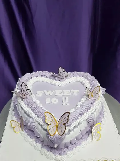 A heart-shaped cake for a Sweet 16. This design features delicate purple and white piping and is adorned with beautiful butterflies, making it a dreamy and romantic choice for a milestone birthday.