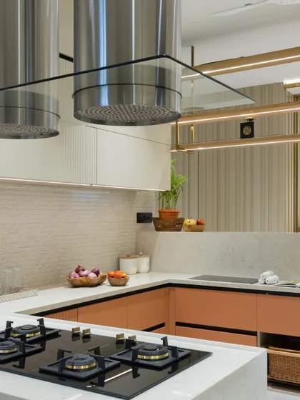 A kitchen where sleek cabinetry, warm neutral tones, and statement hardware come together. The dual stainless steel chimneys add a professional touch to this stylish and functional cooking space.