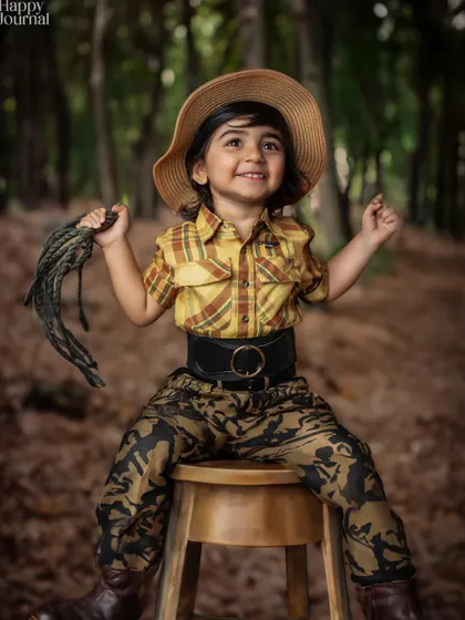 A little cowgirl ready for adventure! Dressed in a plaid shirt, hat, and boots, she sits confidently in a woodland setting.
