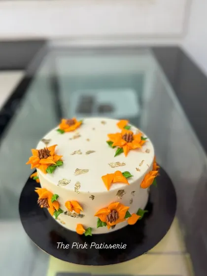 A cheerful cake decorated with bright orange piped sunflowers and flecks of edible silver leaf. This design brings a touch of sunshine to any celebration.