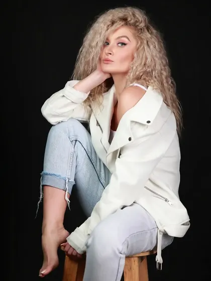 A relaxed and confident portrait of a model with beautiful curly hair. The simple styling with a white jacket and jeans makes this a versatile and classic portfolio shot.