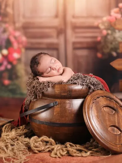 A wider perspective of the newborn in a pot setup. This view shows the full, charming scene with rustic wooden props and a floral background, making the sleeping baby look even more precious.
