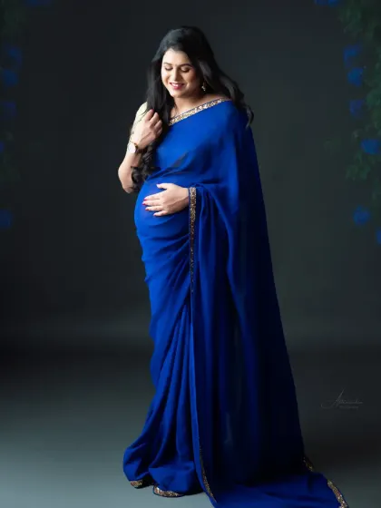 The deep, royal blue of this saree is simply captivating. We love how the soft studio light highlights the fabric's texture and the mom-to-be's gentle expression.
