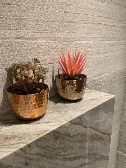 Small hammered copper pots with succulents add a touch of life and metallic warmth to a stone ledge.