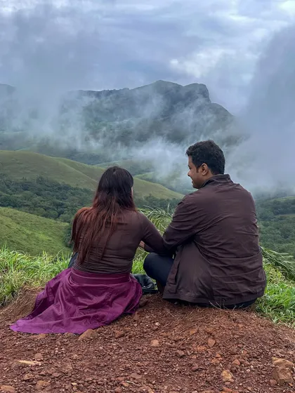 A couple enjoys a quiet moment together, gazing at the misty mountains of Kudremukha. Our treks are perfect for partners who love adventure.