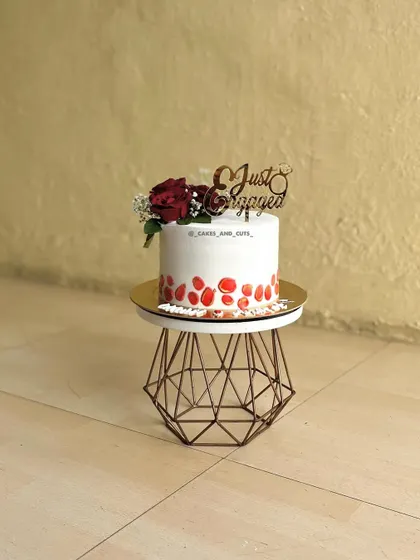 A simple yet elegant single-tier cake for an engagement celebration, decorated with fresh red roses and a beautiful "Just Engaged" topper.
