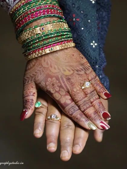 A detailed shot of the couple's hands, showcasing the bride's intricate Mehndi, bangles, and the wedding rings that symbolize their union.