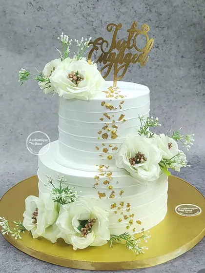Simplicity at its finest. This two-tiered white engagement cake is decorated with beautiful white flowers and a sprinkle of gold flakes, topped with a "Just Engaged" sign.