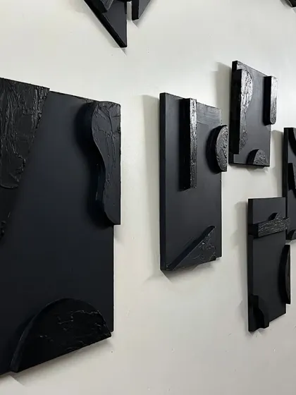 A view of the black multi-panel artwork installed in a Delhi residence. The pieces are arranged to create a dynamic flow across the wall, interacting with each other to form a single installation.