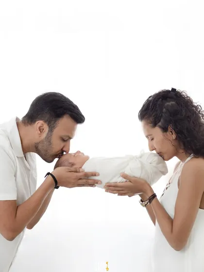 A kiss from mom and dad. This beautiful, high-key portrait shows new parents gently kissing their swaddled newborn, a symbol of their shared love.
