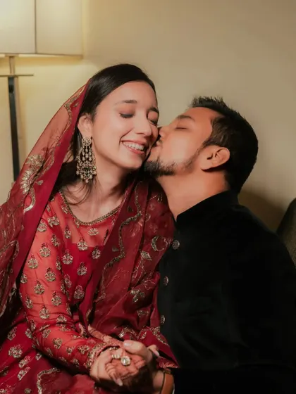 A sweet, candid moment between the happy couple. The bride's minimal makeup and red outfit create a look of effortless grace.