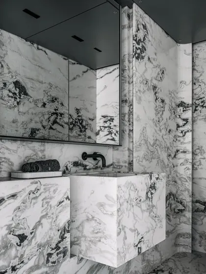 The powder room is a dramatic space finished in Stencil grey marble with a dark grey ceiling and a monolithic built-in basin.