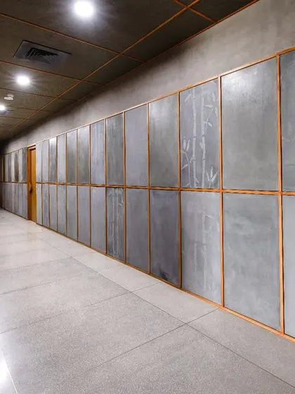 The corridor at Anthea Pharma, featuring terrazzo flooring with brass inlays and cement wall panels etched with bamboo designs. The ceiling is clad in chatai panels, a locally sourced material traditionally used for flooring.
