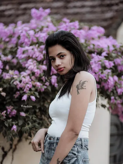 A cool and casual portrait against a wall of purple flowers. The contrast between the simple outfit and the vibrant background makes the image pop.