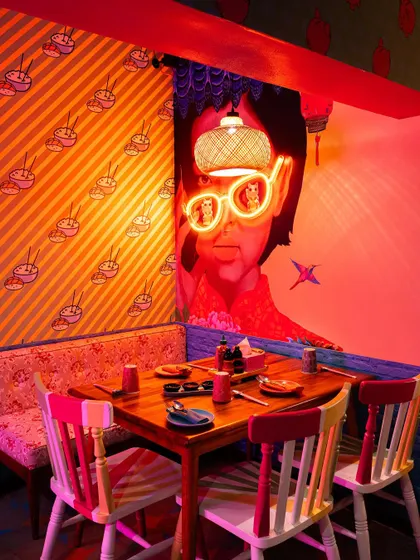 An intimate dining nook at The Fatty Bao, featuring neon-accented wall art. This shot shows customers a specific table, helping them visualize a more private dining experience within the lively restaurant.