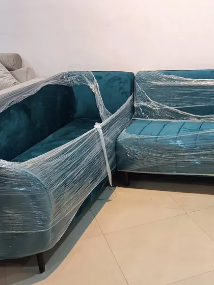 A custom-designed L-shaped sofa in a vibrant teal fabric, wrapped and ready for delivery. We create bespoke furniture tailored to your exact specifications.