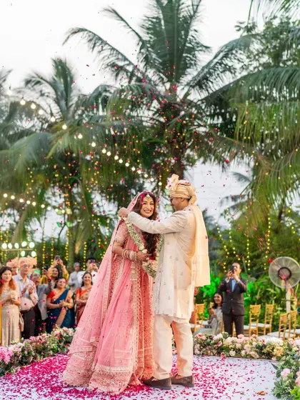 The groom places the varmala on his bride, and their happy expressions are priceless. The surrounding guests add to the celebratory feel.