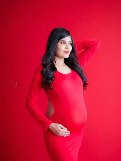 A duplicate of image 162, this bold portrait features a mom-to-be in a striking red dress against a matching red background for a modern feel.