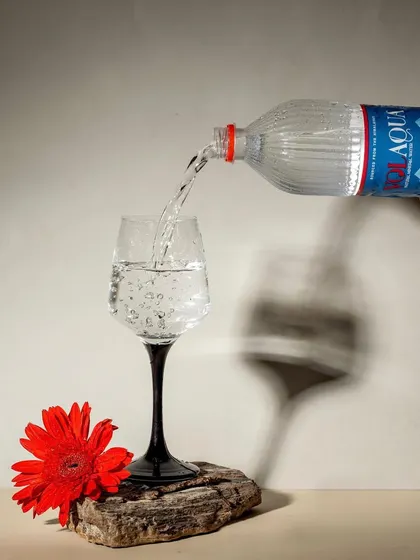 A creative shot of Volaqua water being poured, with a strong, artistic shadow cast on the wall. The single red flower adds a pop of color and a touch of elegance to this minimalist composition.