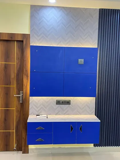 A bold and colorful entryway featuring a blue TV cabinet and a modern wooden flush door with gold inlay.