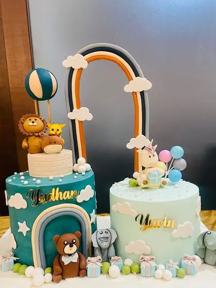 A lovely set of twinning cakes for two birthday boys. One cake has a jungle animal theme, while the other features a unicorn, both connected by a beautiful rainbow.