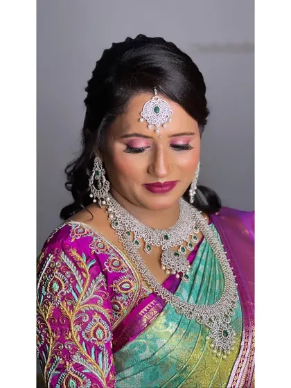 A polished makeup and hair look for a reception. The hair is styled with soft side-swept waves, complementing the modern diamond jewelry and embroidered blouse.