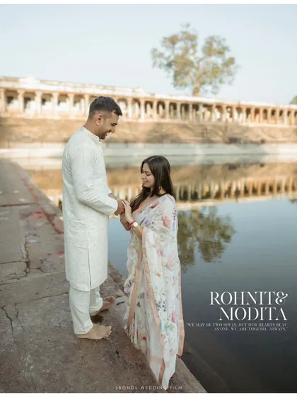 A serene portrait of the couple by the water's edge near a historic temple, dressed in beautiful traditional Indian attire for their pre-wedding shoot.