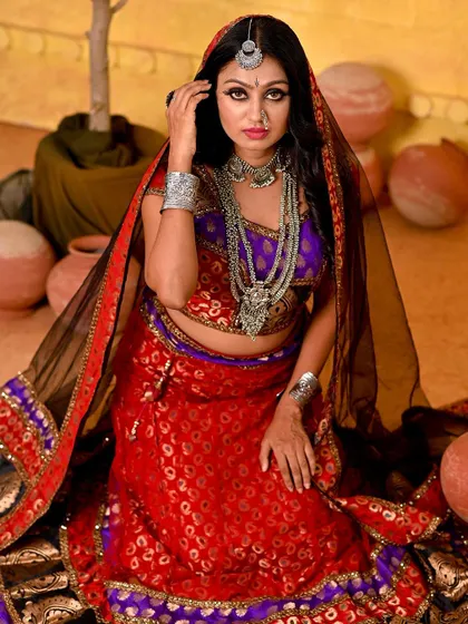 A kneeling pose from the Rajasthani series, showcasing the full, vibrant ghagra. The black veil adds a layer of mystery and tradition to the look.