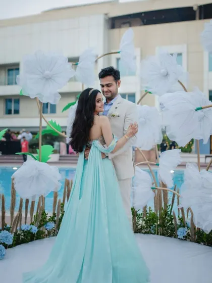 The couple shares a dance in front of a whimsical backdrop of giant paper flowers by the pool, a perfect photo-op at their carnival-themed event.