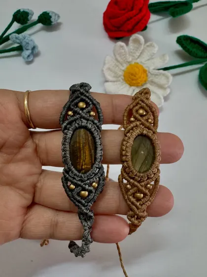 Holding the two macrame bracelets for men to show the intricate knot work and the beautiful central stones.