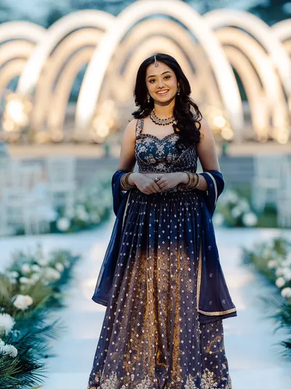The bride looking radiant at her Roce ceremony. She stands before the aisle of modern white arches, which are beautifully lit to create a grand and elegant atmosphere.