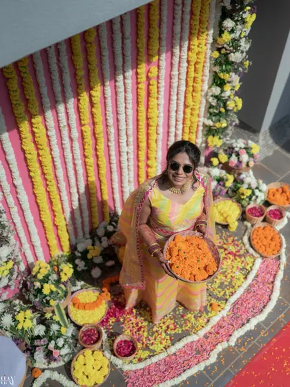 An aerial view of the bride seated amidst a sea of colorful flower petals, holding a bowl of marigolds.