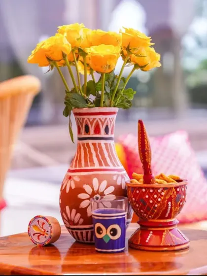 A quirky and traditional centerpiece perfect for a Mehendi. A hand-painted terracotta vase with yellow roses is paired with other colourful, folk-art inspired decorative items.