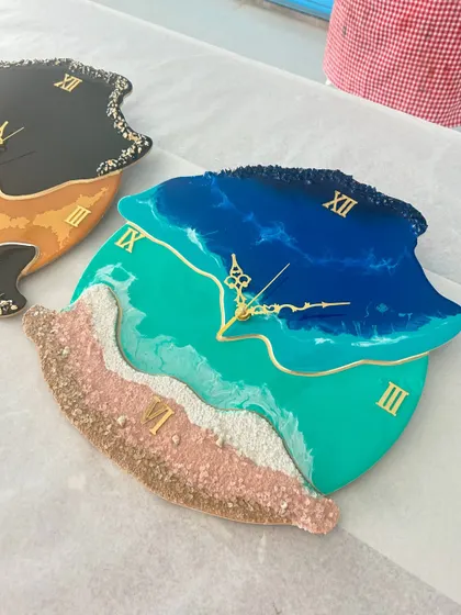 Two unique, free-form resin clocks, one with a beach theme and another with a bold black and orange design, showing the range of styles we teach.