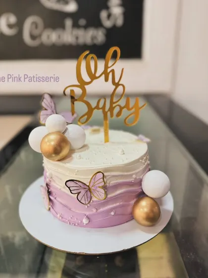A beautiful "Oh Baby" shower cake with a purple ombre wave design. This elegant cake is decorated with gold and white spheres and delicate butterfly accents.