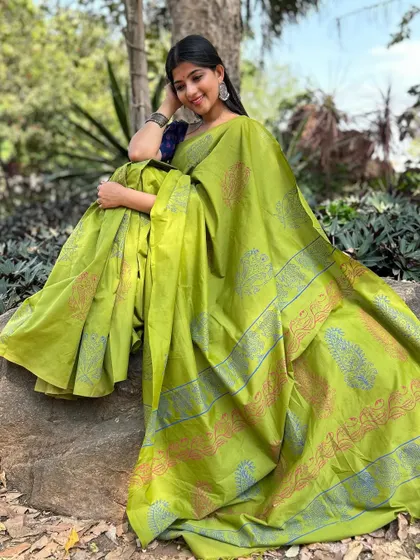 A full-length shot of a vibrant green cotton saree with a contrasting blue blouse. The drape and fall of the fabric are beautifully captured in this outdoor setting.