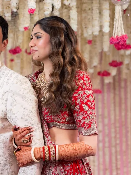 A candid side profile of the bride, showing off her intricate red lehenga and the soft waves in her hair. The makeup is elegant and timeless.