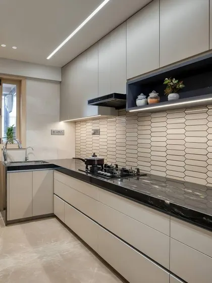 A modern kitchen with off-white cabinets, a black countertop, and a unique hexagonal tile backsplash. The linear lighting under the cabinet provides excellent task lighting for cooking.