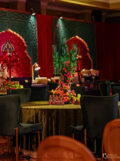 A guest dining table with a unique green glass candelabra centerpiece surrounded by flowers. The background shows the continued use of red and green architectural elements throughout the space.