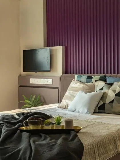 A cozy reading nook by the window in a master bedroom. The design features a vibrant purple fluted panel behind the bed, adding a pop of color and texture to the neutral space.